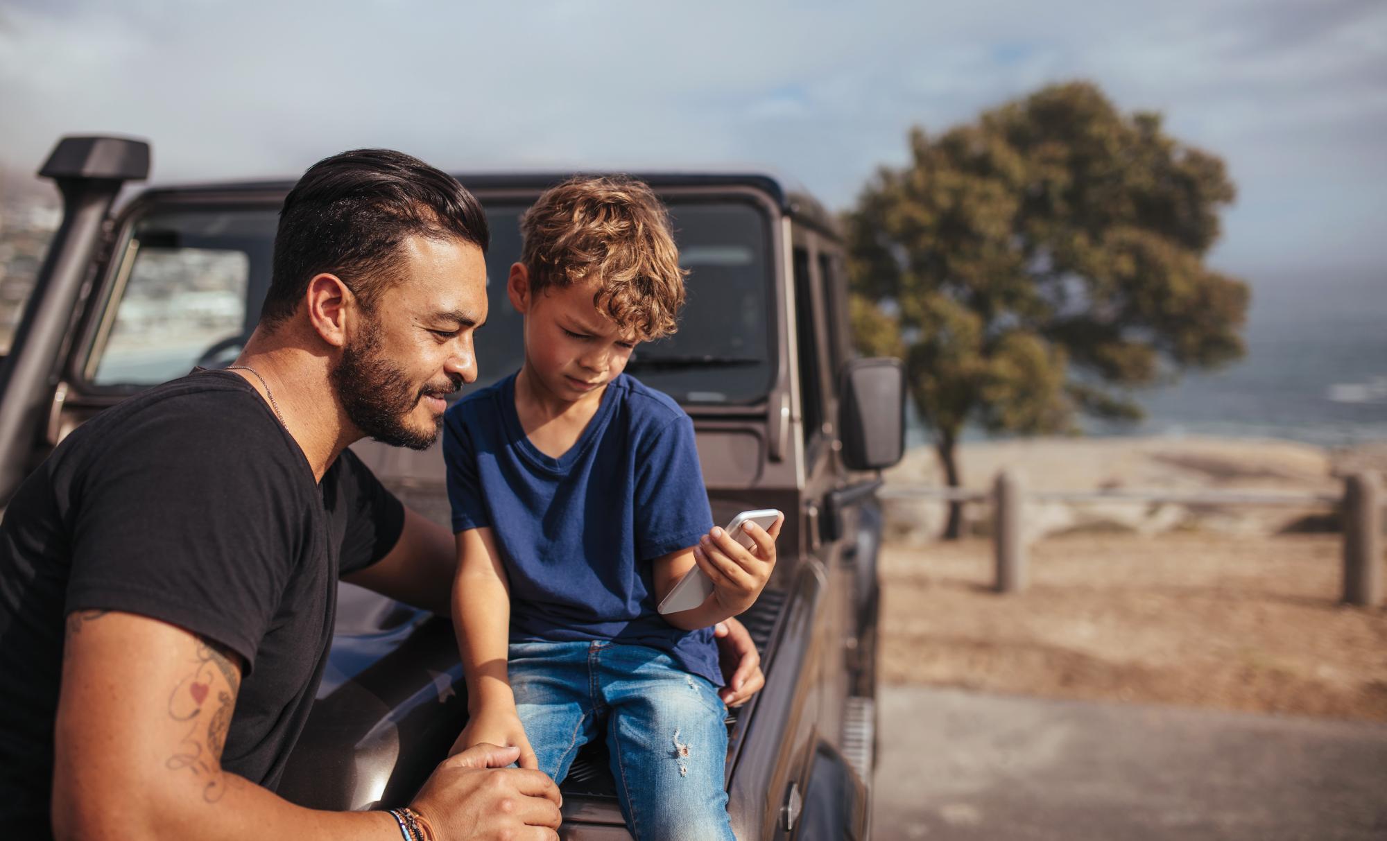 A young boy sitting on a car with a phone